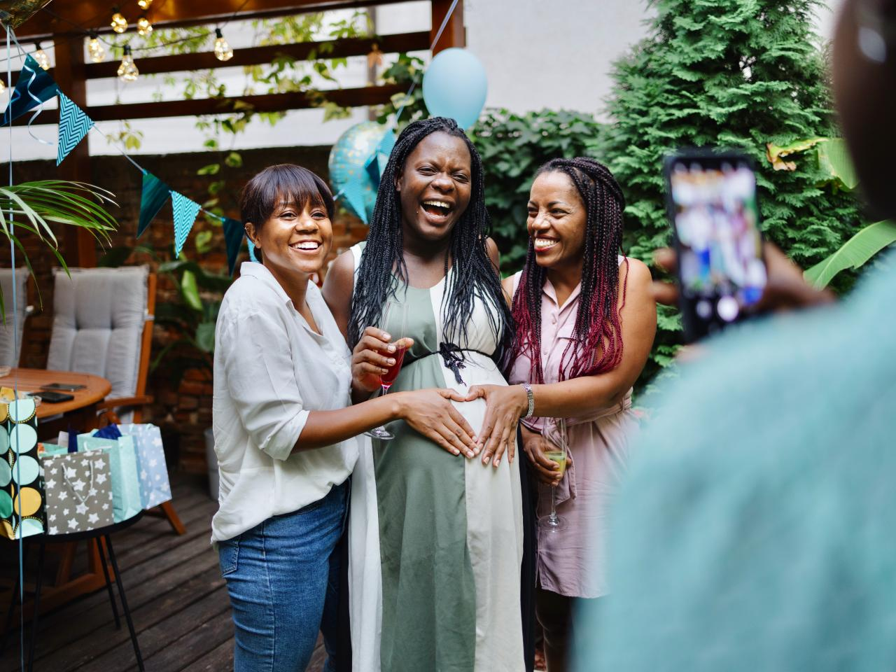 Friends laughing around a mom-to-be at an outdoor baby shower