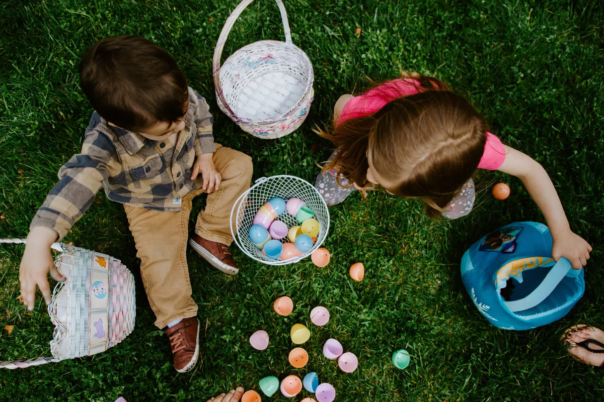 Two children sitting on the grass during an Easter egg hunt with baskets and colorful eggs