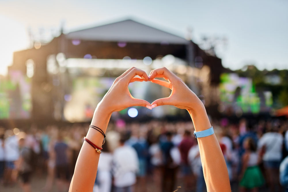 Hands forming a heart in front of a festival stage at sunset