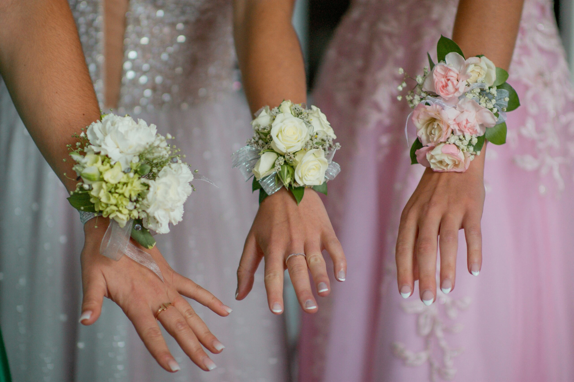 Trois jeunes filles en robes pastel portant des bracelets fleuris au bal de promo