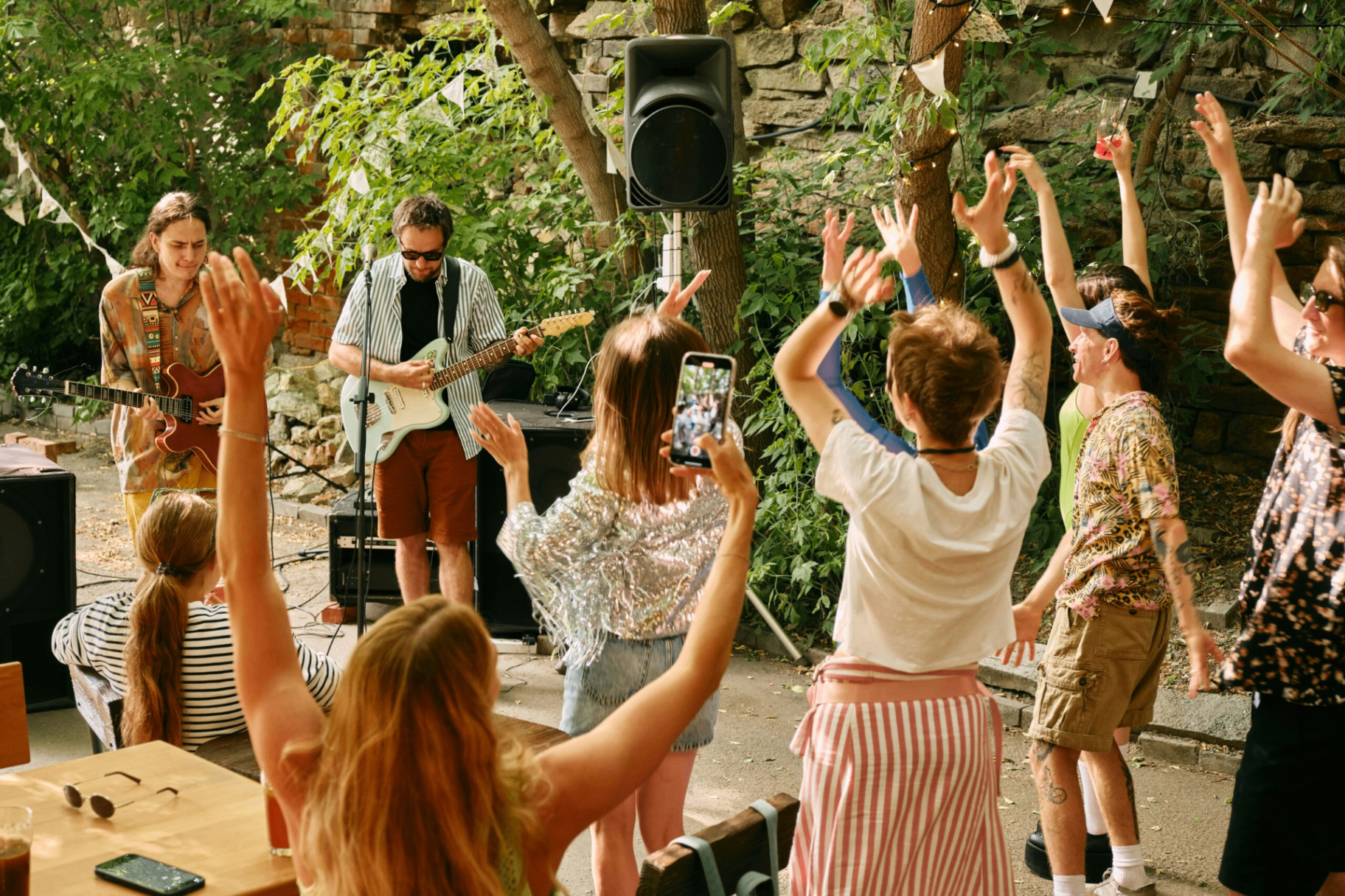 Crowd dancing with arms raised in front of a live band at an outdoor village fair
